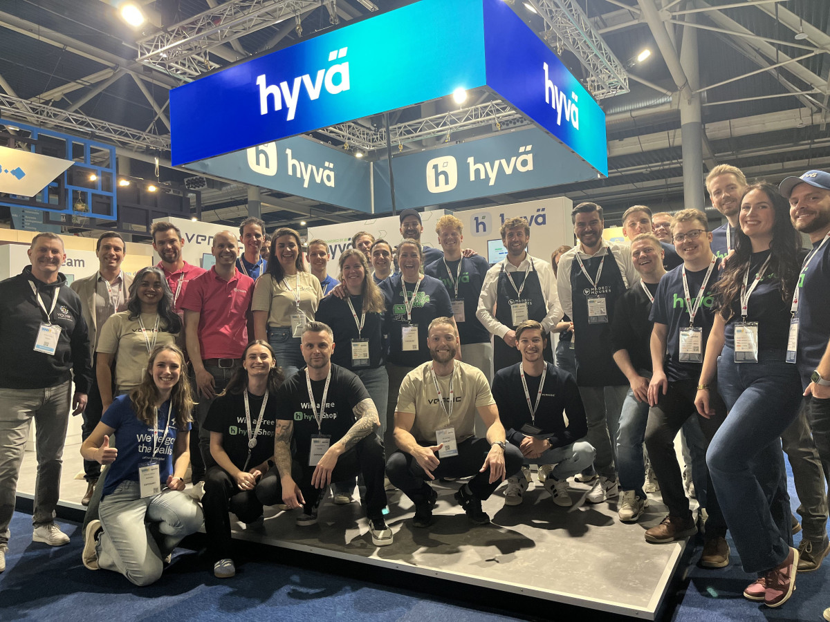 Large group photo at a Hyva-branded trade show booth, with Hyva signage overhead.