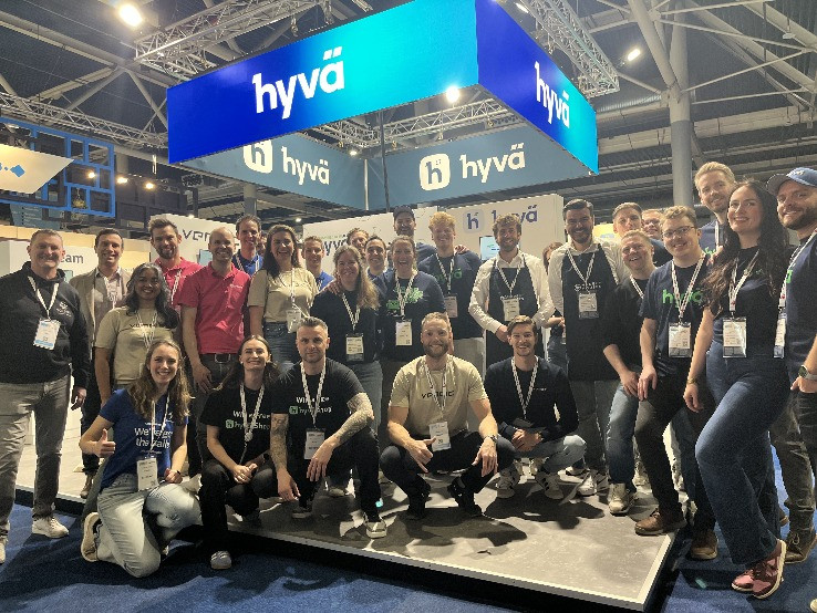 Large group photo at a Hyva-branded trade show booth, with Hyva signage overhead.