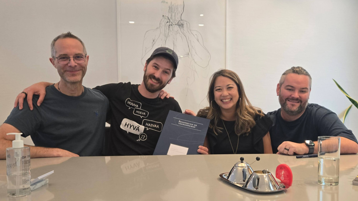 Four people seated at a table smiling, one holding a document, in a casual office setting