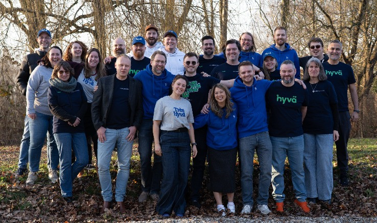Group photo of Hyva team members standing outdoors in a wooded area, wearing Hyva-branded clothing